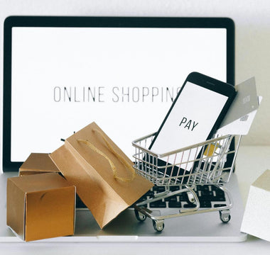A laptop holds tiny cardboard boxes and shopping carts