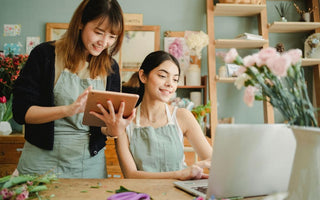 Happy multiracial women working on gadgets in floral store 