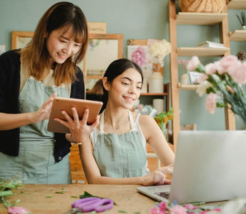 Happy multiracial women working on gadgets in floral store 